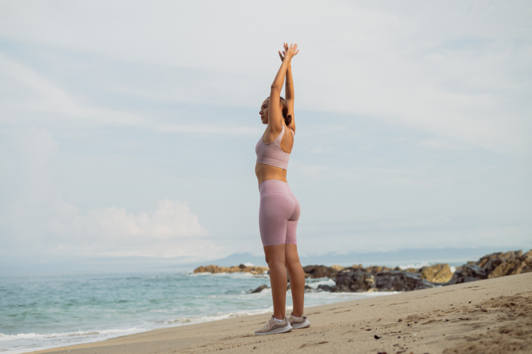 fit woman stretching on the beach happy because she learnt how to break through a weight loss plateau and reach her fitness goals